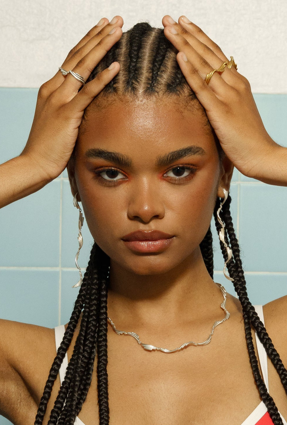 A person with braided hair wearing the suave earrings long, which are long and have a silver color with gold plating accents.